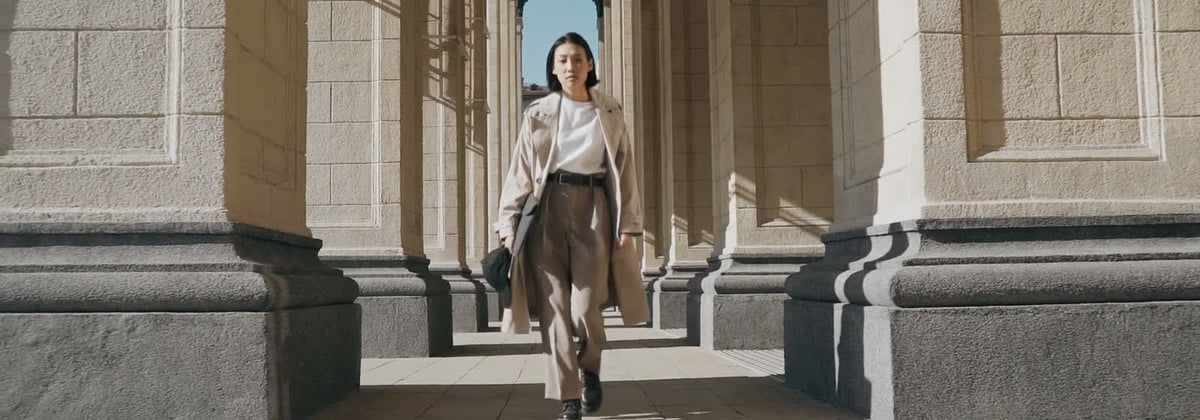 Femme élégante en trench et pantalon fluide marchant sous une colonnade