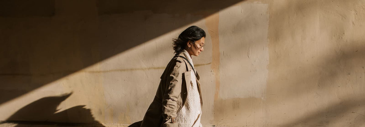 Femme en trench beige léger marchant le long d'un mur ensoleillé