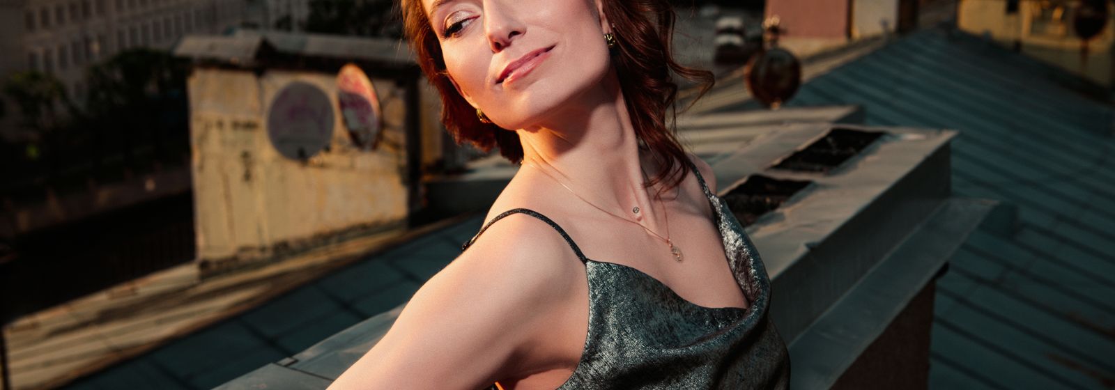 Femme élégante en robe à bretelles sur un rooftop au coucher du soleil — tenue de soirée d'été Vogue Française