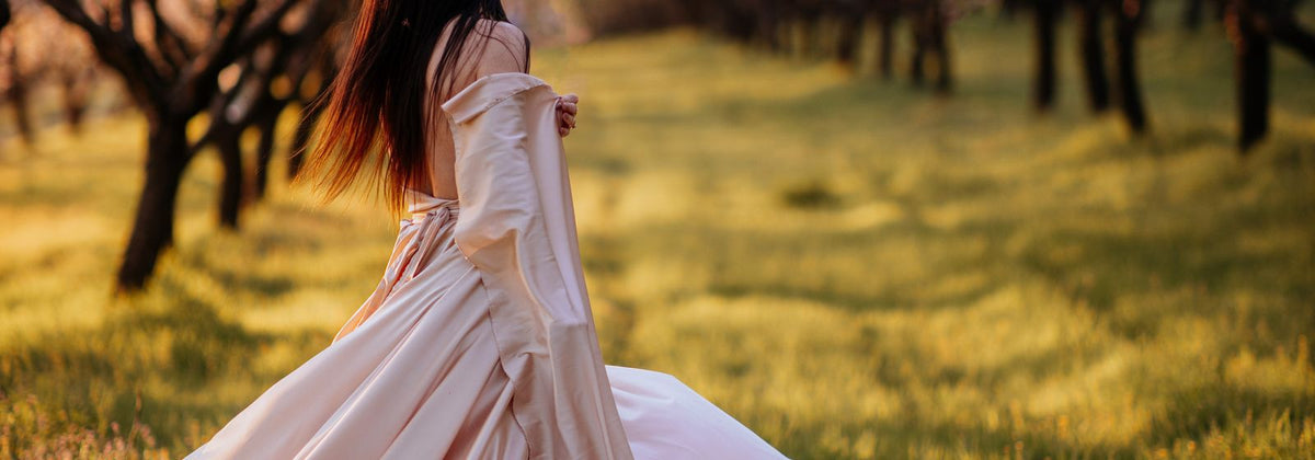 Femme en robe longue fluide dans un verger à la lumière dorée de fin de journée
