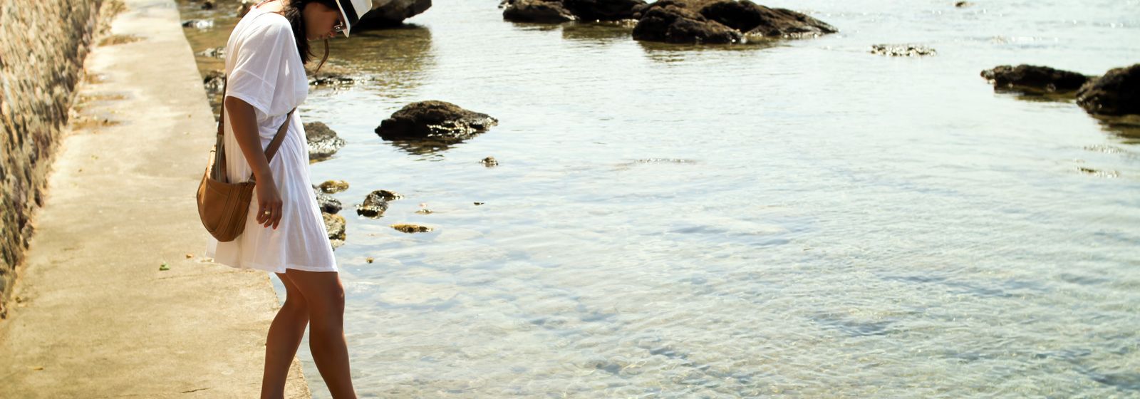 Femme en robe blanche au bord d'une eau turquoise — porter le blanc en été, Vogue Française